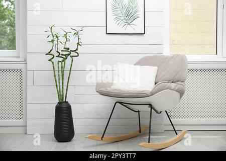 Vase mit grünen Bambusstielen und stilvollem Schaukelstuhl im Zimmer. Innendesign Stockfoto