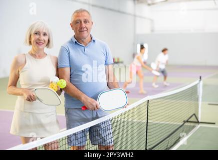 Ältere Ehepaare mit Schlägern und Bällen, die auf dem Pickleball-Platz posieren Stockfoto