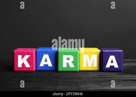 Word Karma aus bunten Würfeln mit Buchstaben auf schwarzem Holztisch Stockfoto