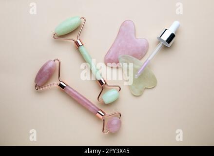 Gua sha Werkzeuge, Gesichtsrollen und Tropfer auf beigefarbenem Hintergrund, flach liegend Stockfoto
