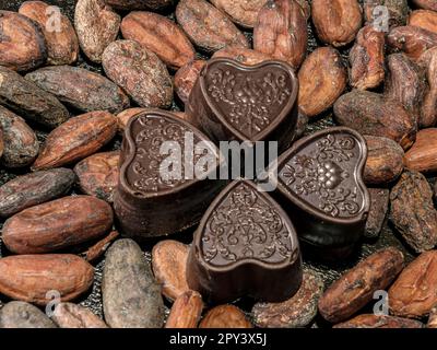 Vier Schokoladen in Herzform auf dem Hintergrund gerösteter Kakaobohnen. Stockfoto