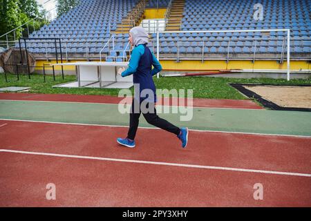 Eine muslimische Frau in einer Burka sportlich muslimische Kleidung, die auf einem Marathonkurs läuft und sich auf die nächsten Wettkämpfe vorbereitet Stockfoto