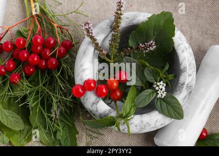 Marmormörtel mit verschiedenen Kräutern, Beeren und Stößel auf Stoff, Draufsicht Stockfoto