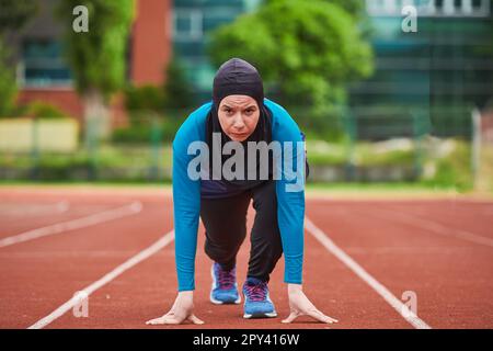 Muslimische Frau in Burka in sportlicher muslimischer Kleidung in Startposition zum Laufen Stockfoto