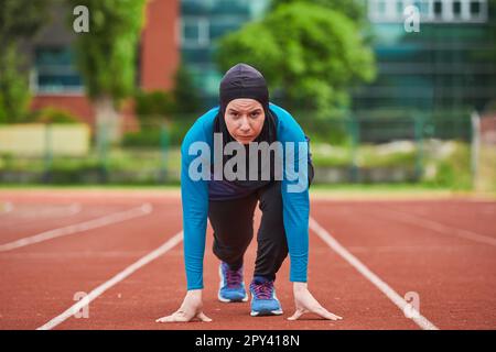 Muslimische Frau in Burka in sportlicher muslimischer Kleidung in Startposition zum Laufen Stockfoto