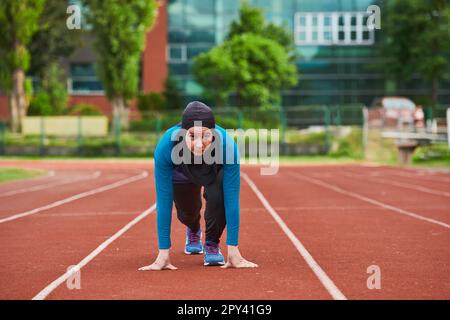 Muslimische Frau in Burka in sportlicher muslimischer Kleidung in Startposition zum Laufen Stockfoto