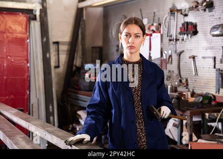 Porträt einer jungen lächelnden Frau in Uniform, die mit einem Hammer in der Hand Stockfoto