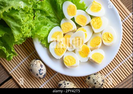 Gekochte Eier Essen, Wachteleier auf weißem Teller, Frühstückseier mit frischen Wachteleiern und Gemüsesalat auf dem Tisch Hintergrund - Draufsicht Stockfoto