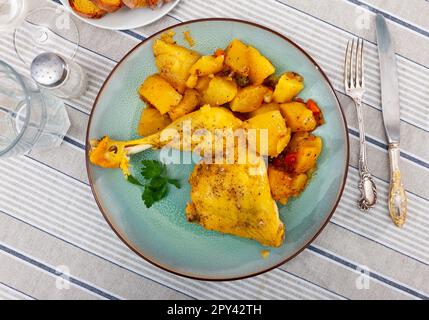 Gebackene Hühnerschenkel mit Bratensoße garniert mit Petersilie und gedünsteter Kartoffel und Karotte Stockfoto