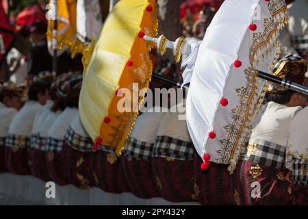 Junge Männer in balinesischen Kostümen, Sarong mit traditionellen Regenschirmen, bezahlt. Hinduistische religiöse Zeremonie. Kunst und Kultur der Insel Bali in Indones Stockfoto