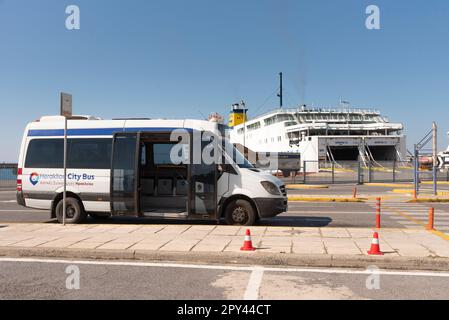 Heraklion, Kreta, Griechenland, EU. 2023. Ein Stadtbus von Heraklion, der im Hafen auf Passagiere wartet, mit einer Fährenlandschaft. Stockfoto