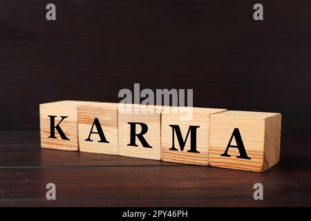 Word Karma aus Würfeln mit Buchstaben auf schwarzem Holzhintergrund Stockfoto