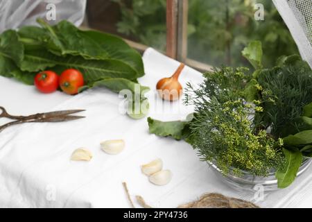 Frische grüne Kräuter, Tomaten, Knoblauchzehen und Zwiebeln auf dem Tisch im Haus Stockfoto