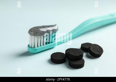Bürsten Sie mit Holzkohle-Zahnpasta und Tabletten auf hellem Hintergrund, Nahaufnahme Stockfoto
