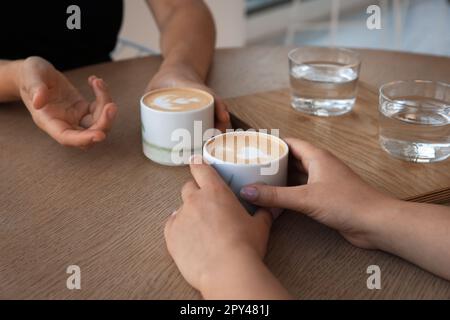 Freunde trinken Kaffee an einem Holztisch im Café, schließen Stockfoto