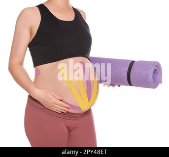 Sportliche schwangere Frau mit Kinesio-Bändern, die Yoga-Matte auf weißem Hintergrund halten, Nahaufnahme Stockfoto