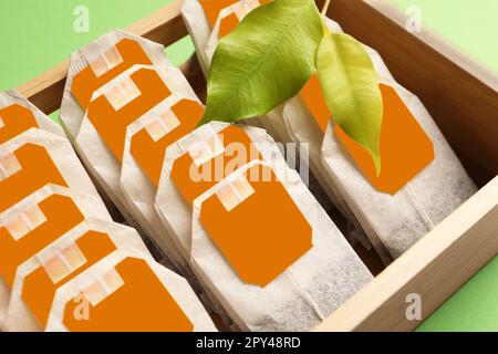 Viele Teebeutel in einer Holzbox und Blätter auf hellgrünem Hintergrund, Nahaufnahme Stockfoto