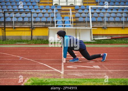 Muslimische Frau in Burka in sportlicher muslimischer Kleidung in Startposition zum Laufen Stockfoto