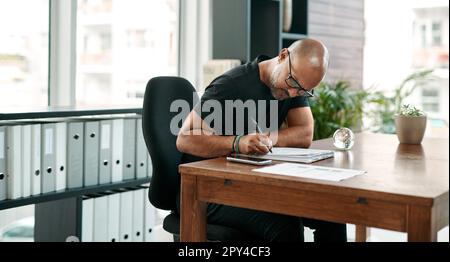 Ein winziges Detail kann das gesamte Design verändern. Ein reifer Geschäftsmann, der Papierkram an seinem Schreibtisch in einem modernen Büro ausfüllt. Stockfoto