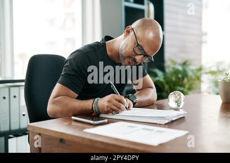 Er kennt seine Marke wie seine Westentasche. Ein reifer Geschäftsmann, der Papierkram an seinem Schreibtisch in einem modernen Büro ausfüllt. Stockfoto