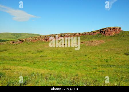 Überreste einer zerstörten alten roten Sandsteinmauer, die an einem klaren Sommertag den Hang hinauf zum Gipfel eines hohen sanften Hügels führt. Bergketten, Kha Stockfoto