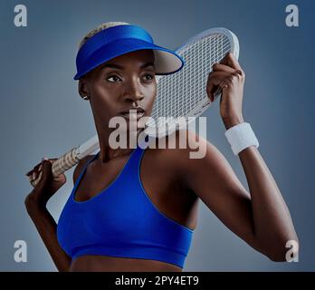 Du kannst alles tun, was du willst. Studioaufnahme einer sportlichen jungen Frau, die mit einem Tennisschläger posiert, vor einem grauen Hintergrund. Stockfoto