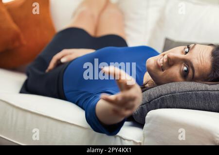 Eine Frau liegt in ihrer Freizeit auf ihrem weißen Sofa, umgeben von orangefarbenen Kissen. Sie trägt ein blaues Hemd und einen schwarzen Minirock. Sie dehnt h aus Stockfoto