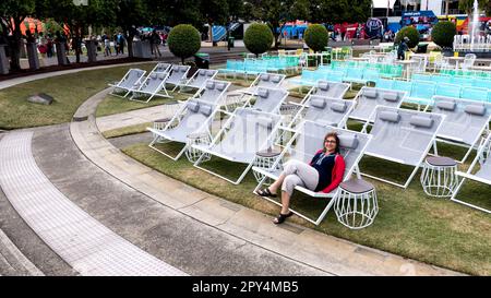 Eine junge Frau entspannt sich in einem Außenpool im Resortstil mit Chaiselongue Stockfoto