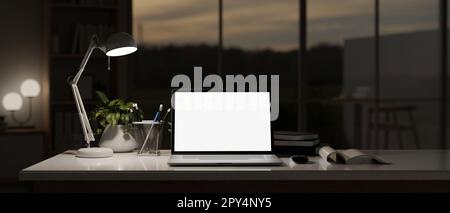 Nahaufnahme eines dunklen Arbeitsplatzes mit weißem Laptop-Mockup, Licht von Tischleuchte und Zubehör auf einem Tisch im Büro bei Nacht. Stockfoto