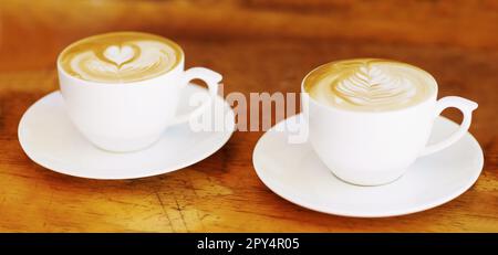 Latte, Retro und Kaffeetasse auf einem braunen Holztisch in einem Restaurant, um Espresso in der Küche zu trinken. Café, Kaffee und Vintage Hintergrund und Espresso Stockfoto