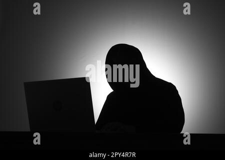 Mysteriöser Mann mit schwarzem Kapuzenpulli, der seinen Laptop benutzt und seine Kreditkarte in der Dunkelkammer hält. Hacker- und Cybersicherheitskonzept. Stockfoto