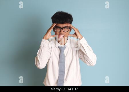 Indonesische Oberschülerin in weißer Hemduniform mit grauer Krawatte, schreiend mit geschlossenen Augen und offenem Mund, Hände an der Stirn Stockfoto