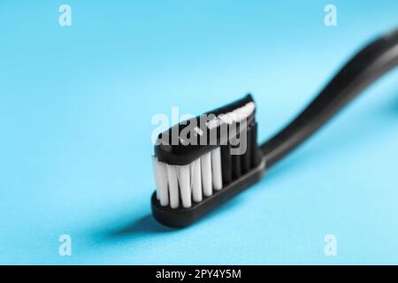 Bürste mit dunkelkohlensäurehaltiger Zahnpasta auf hellblauem Hintergrund, Nahaufnahme Stockfoto