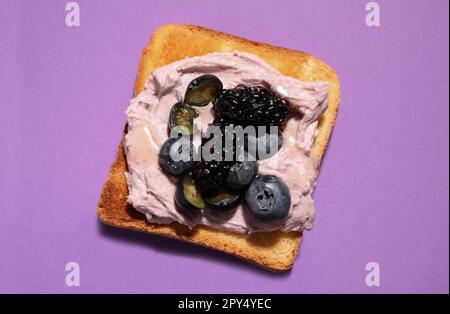 Leckeres Sandwich mit Frischkäse, Brombeeren und Blaubeeren auf lila Hintergrund, Draufsicht Stockfoto