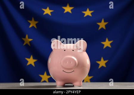 Pinkfarbenes Sparschwein auf hellgrauem Tisch gegen die Flagge der Europäischen Union Stockfoto