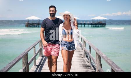 Wir waren noch nie überall, aber es steht auf unserer Liste. Ein glückliches, junges Paar, das Arm in Arm während eines gemeinsamen Urlaubs eine Promenade hinuntergeht. Stockfoto