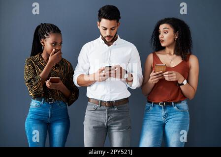Oh, mein Gott! Ein gutaussehender junger Geschäftsmann, der im Studio steht und sein Handy benutzt, während seine Kollegen ihn beobachten. Stockfoto