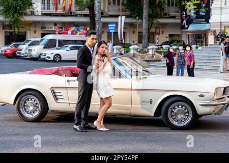 Braut und Bräutigam posieren mit einem 1967 Ford Mustang Cabrio, das als Hochzeitsauto vor dem Opernhaus, Ho Chi Minh City, Vietnam, verwendet wurde Stockfoto