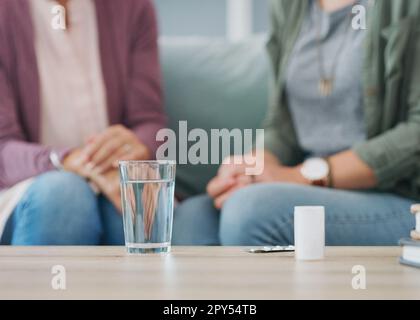 So sieht das Seniorenheim aus. Zwei unbekannte Frauen sitzen auf dem Sofa mit einem Pillbox und Wasser im Wohnzimmer. Stockfoto