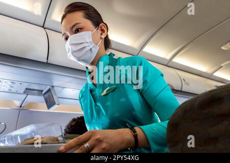 Vietnam Airlines Kabinenpersonal kümmert sich um die Passagiere, trägt AO dai Uniform auf dem Flug von Bangkok nach Vietnam Stockfoto