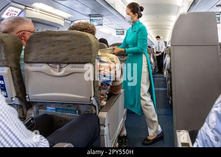 Vietnam Airlines Kabinenpersonal kümmert sich um die Passagiere, trägt AO dai Uniform auf dem Flug von Bangkok nach Vietnam Stockfoto