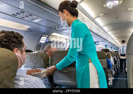 Vietnam Airlines Kabinenpersonal kümmert sich um die Passagiere, trägt AO dai Uniform auf dem Flug von Bangkok nach Vietnam Stockfoto