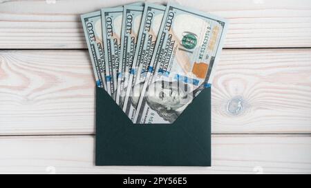 Ein flacher grüner Umschlag mit einem 100-Dollar-Banknotenschein auf einem grauen Holztisch. Korrespondenz, Geld. Stockfoto