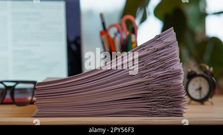 Zusammenstellung eines Stapels von Papieren, sortiert mit Büroklammern, Gläsern, Uhr, Büromaterial in der Nähe des Laptops auf dem Schreibtisch. Arbeitsbereich. Stockfoto