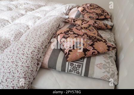 Pinke dekorative Kissen auf der Bettwäsche. Doppel-Hochzeitsbett mit Kissen und dicker Federdecke. Schlafzimmerdesign. Weiches weißes Kopfteil. Einrichtung mit Möbeln und Bettwäsche. Stockfoto