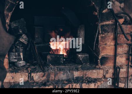 Alter Ziegelofen mit brennender Flamme in Schmiede. Herstellung von Eisen im Rußkamin in der Werkstatt. Metallarbeiten, Schmieden. Stockfoto