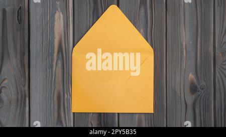 Flaches Verlegen eines offenen leeren gelben Umschlags auf einem grauen Holztisch. Korrespondenz, Post, Post, Büromaterial, Einladung. Stockfoto