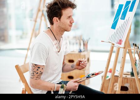 Kreativität kommt nie aus der Mode. Ein gutaussehender junger Künstler, der allein sitzt und während eines Kunstkurses im Studio malt. Stockfoto