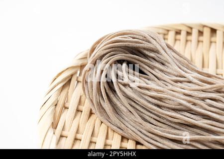 Rohe Soba-Nudeln in einem Bambussieb vor weißem Hintergrund. Stockfoto