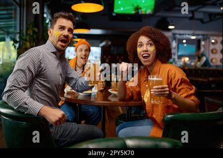 Freunde von Fußballfans mit kreativem Make-up im Pub anfeuern Stockfoto